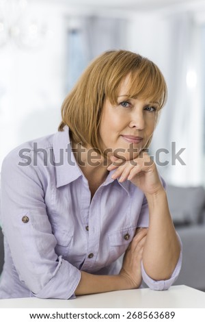 Portrait of mature woman with hand on chin sitting at table in house