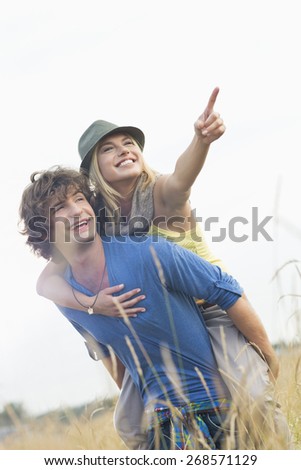 Cheerful woman showing something while enjoying piggyback ride on man in field