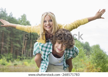 Portrait of happy woman enjoying piggyback ride on man in forest