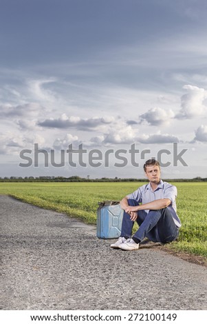 Full length of young man with empty petrol can sitting by country road
