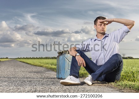 Full length of young man shielding eyes while sitting with petrol can by country road