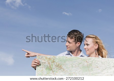 Young man holding map while woman pointing away against sky