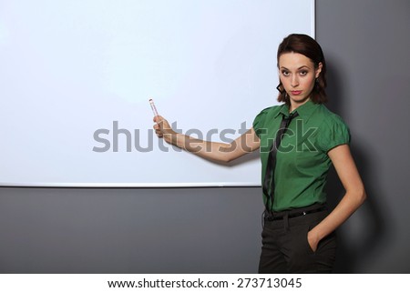 Portrait of businesswoman with hands in pockets pointing at whiteboard in office
