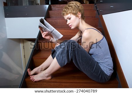 Young woman reading newspaper on stairs
