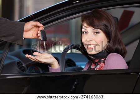 Portrait of young woman receiving the car keys from car salesman