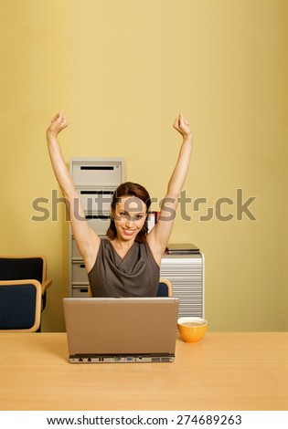 Portrait of businesswoman with arms raised, cup and laptop on desk