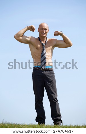 Portrait of shirtless bald young man wearing tie holds his arms up in park
