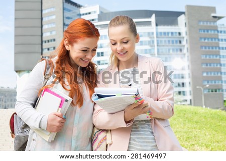 Happy young female college students studying in park with building in background