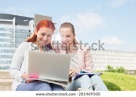 Smiling young university students using laptop with buildings in background