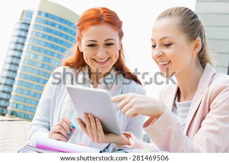 Smiling young university students using digital tablet against building
