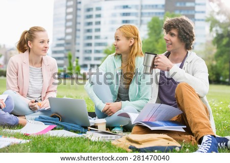 Young man having coffee while studying with female friends at college campus