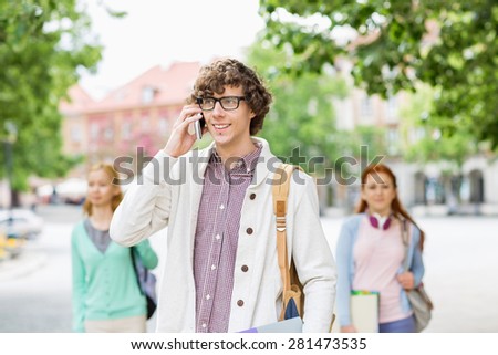 Smiling young male student using cell phone with friends in background on street