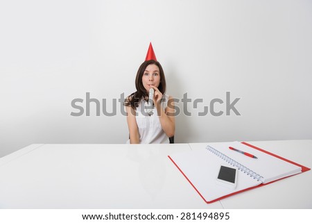 Portrait of happy businesswoman in party hat blowing horn at desk in office