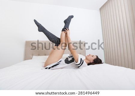 Full length side view of young woman wearing socks while lying in bed