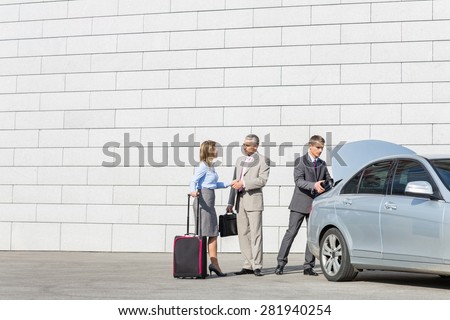 Businesspeople with luggage shaking hands outside car on street