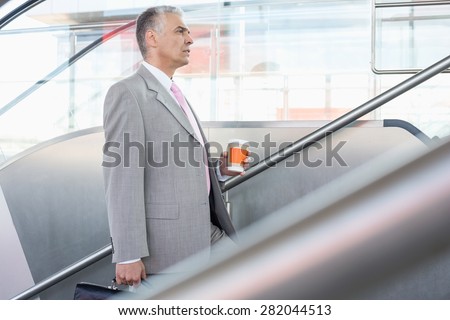Side view of middle aged businessman with coffee cup walking up stairs in railroad station