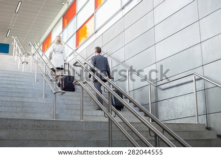 Rear view of businessman and businesswoman with luggage moving upstairs in railroad station