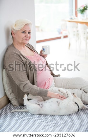 Portrait of happy senior woman having coffee while stroking dog at home