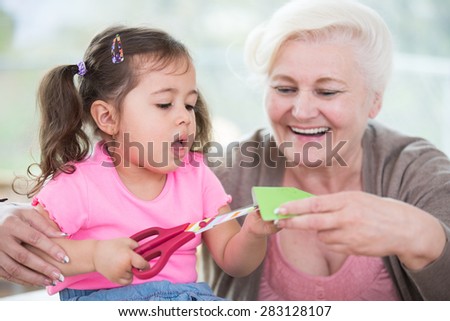 Senior woman with granddaughter cutting paper at home