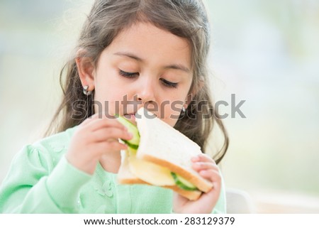 Cute girl eating sandwich at home