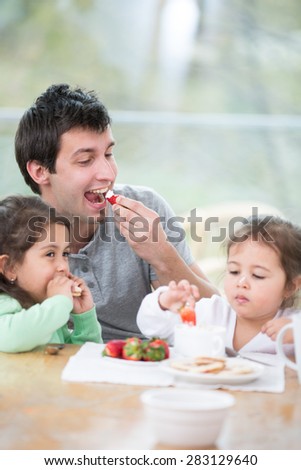 Father and daughters eating strawberries with whipped cream at home