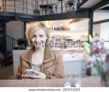 Portrait of happy young woman using cell phone in cafe