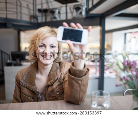 Portrait of smiling young woman displaying cell phone in cafe