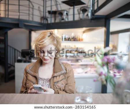 Happy young woman reading text message on cell phone in cafe