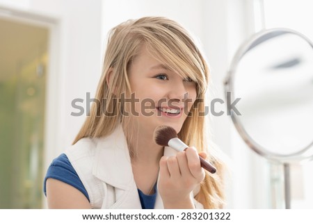 Girl applying makeup in front of mirror at home