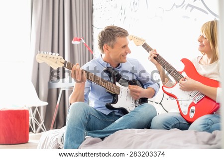 Happy father and daughter playing guitars at home