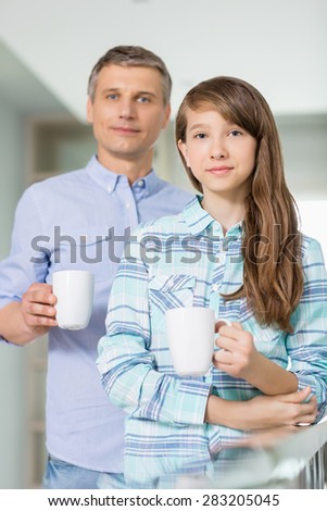 Portrait of father and daughter holding coffee cups at home