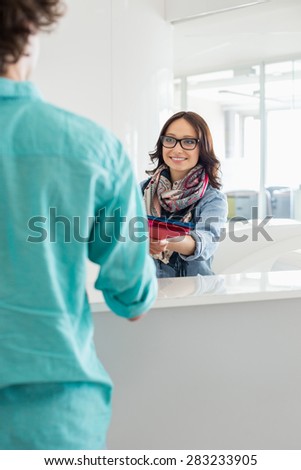 Smiling businesswoman handing over to male colleague at counter in creative office