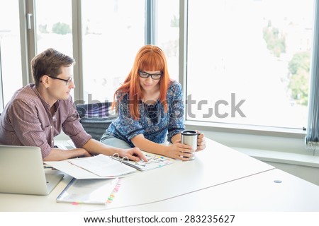 Creative business colleagues reading file together at desk in office