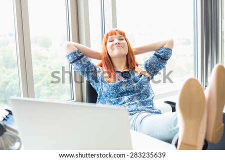 Businesswoman relaxing with feet up at desk in creative office