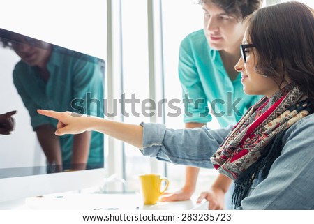 Creative businesswoman showing something to colleague on desktop computer in office