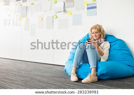 Smiling businesswoman using mobile phone on beanbag chair in creative office