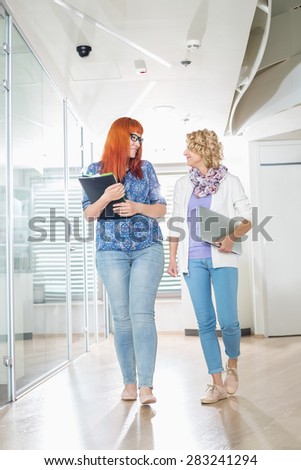 Full-length of creative businesswomen conversing while walking at office hallway