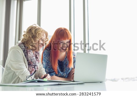 Happy creative businesswomen using laptop together in office