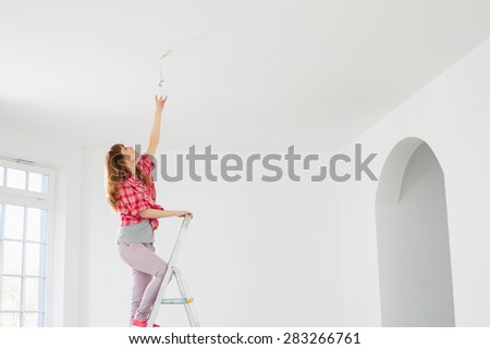 Full-length of woman on ladder fitting light bulb in new house