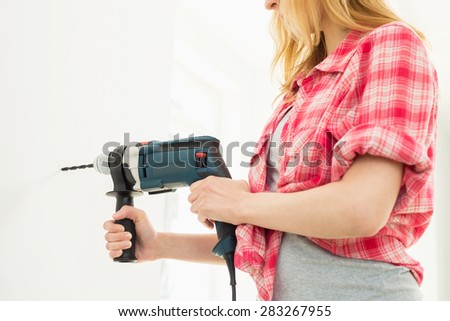 Midsection of woman drilling wall in new house
