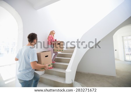 Couple carrying moving boxes up stairs in new house