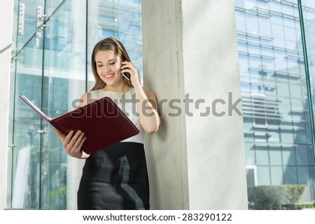 Happy businesswoman using cell phone while reading file in office
