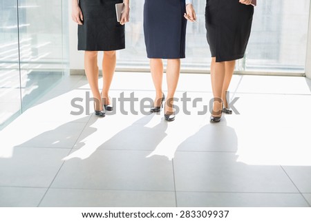 Low section of businesswomen standing on tiled floor in office