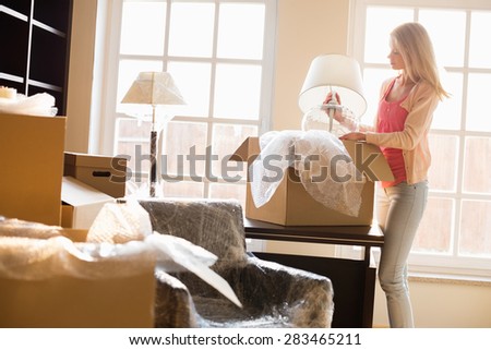 Woman removing lamp from moving box at new house