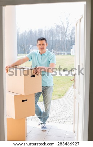 Full-length portrait of man with stacked cardboard boxes at new house