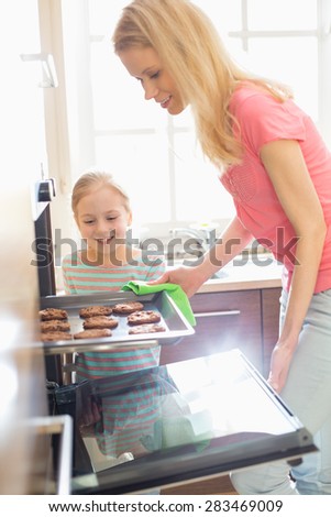 Happy mother and daughter removing cookie tray from oven at home