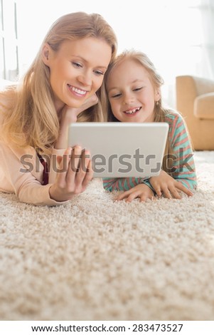 Happy mother and daughter using digital tablet on floor at home