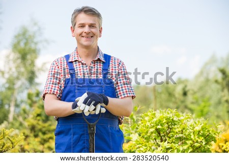 Portrait of happy gardener holding spade in plant nursery