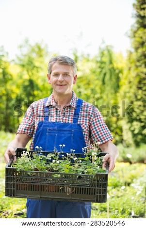 Portrait of smiling man holding crate of potted plants at garden