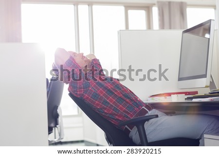Side view of young businessman relaxing at computer desk in office